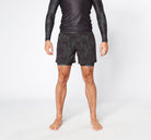 A barefoot man is standing against a plain white background, wearing a black long-sleeve athletic shirt and FADED SABBATH SHORTS by Divine JiuJitsu. His hands are relaxed by his sides, and his head is not visible in the frame.