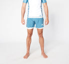 A person wearing a light blue and white athletic outfit, featuring a short-sleeved shirt and Divine JiuJitsu's STEEL BJJ SHORTS made from sustainable materials. The individual stands barefoot on a light background with arms relaxed at their sides, with only the lower half of their head visible in the frame.