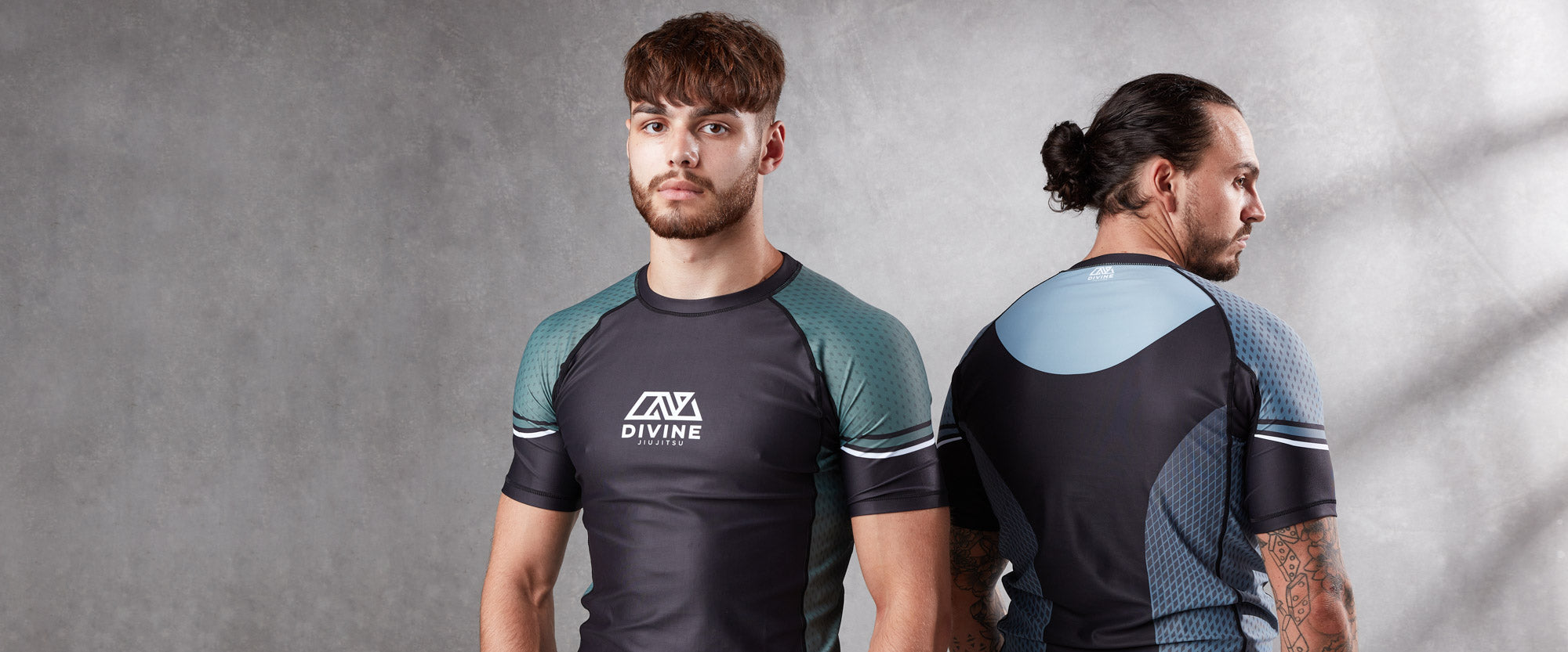 Two men are modeling athletic wear. The man on the left faces forward, wearing a short-sleeve shirt with the "Divine" logo on the chest. The man on the right has a man bun and faces away, showing the back of the shirt which features a light blue panel.